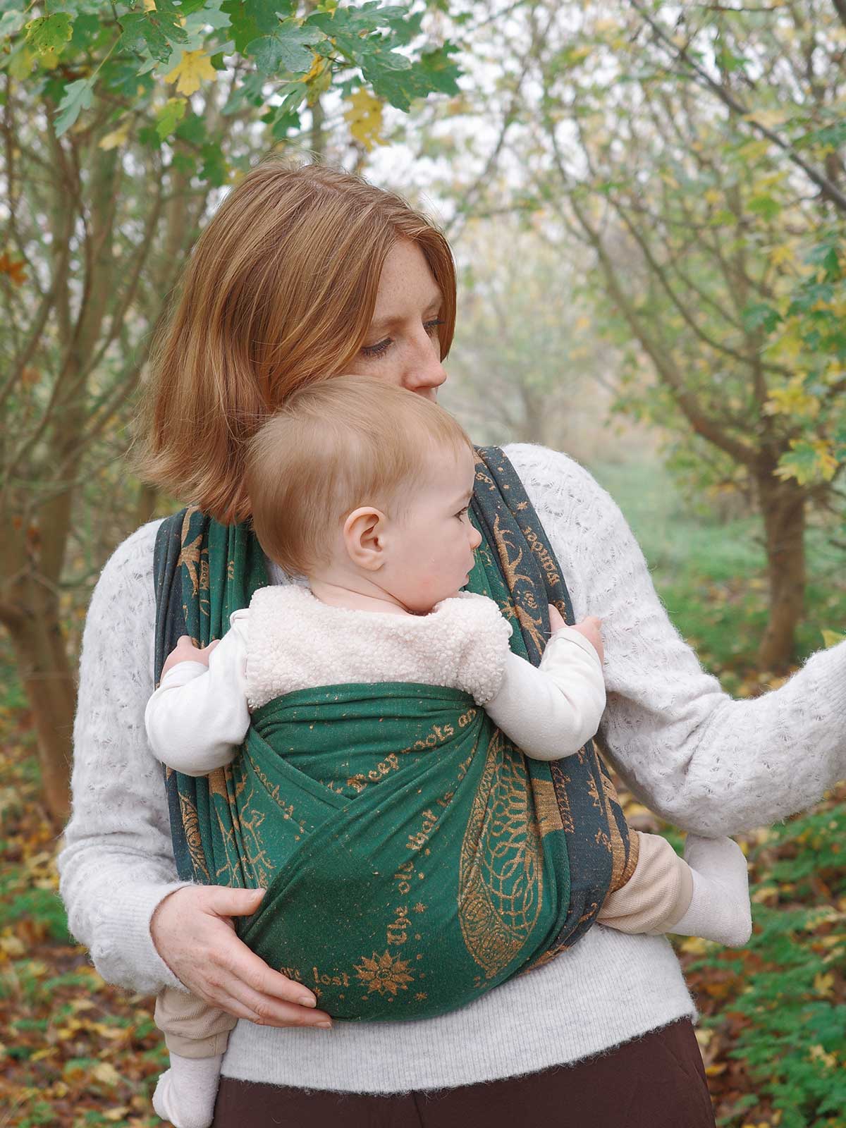 Woman carrying a baby in a green baby wrap with a forest background