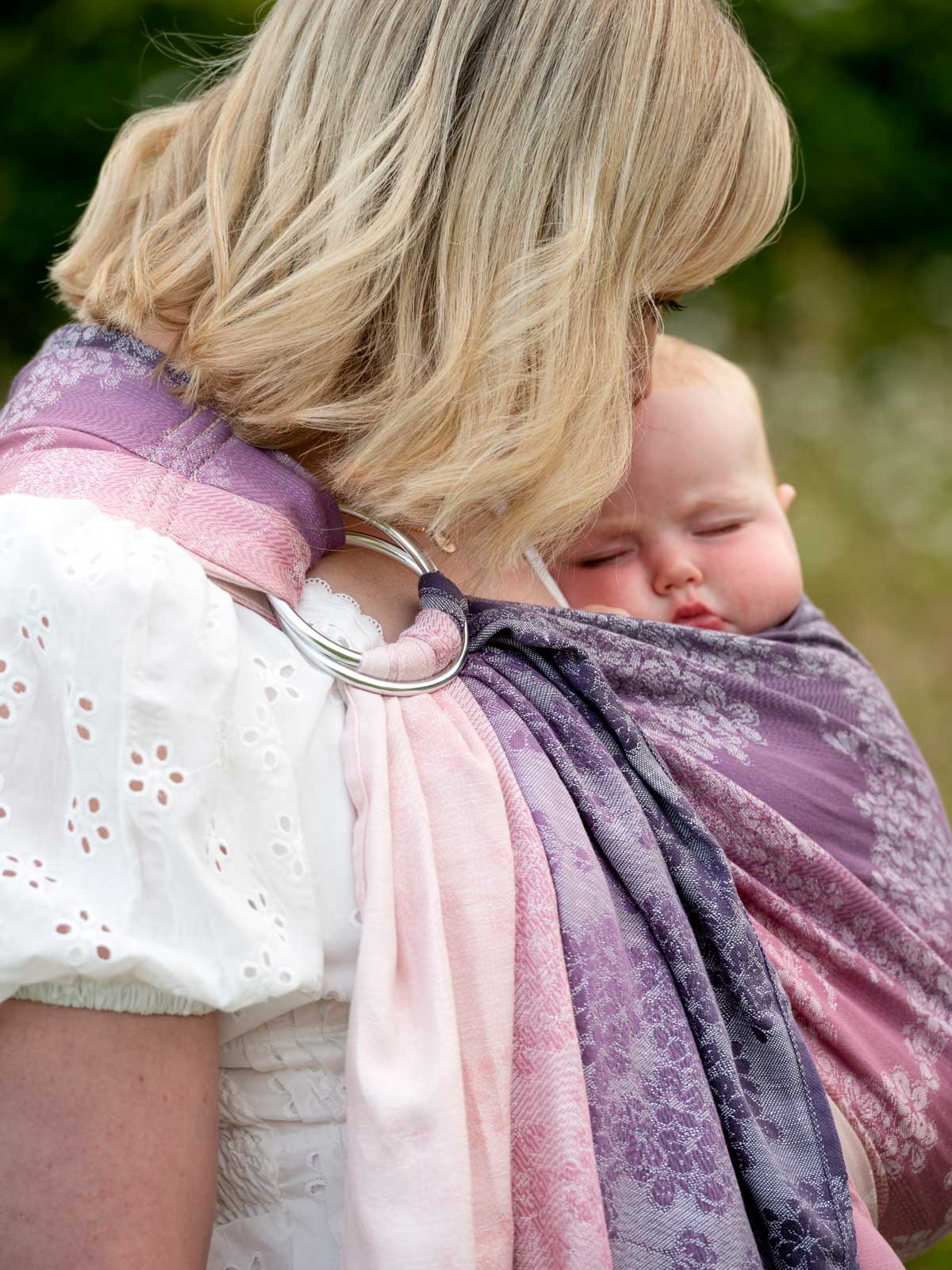 Detail of baby ring sling carrier in soft pink and purple blossom pattern.