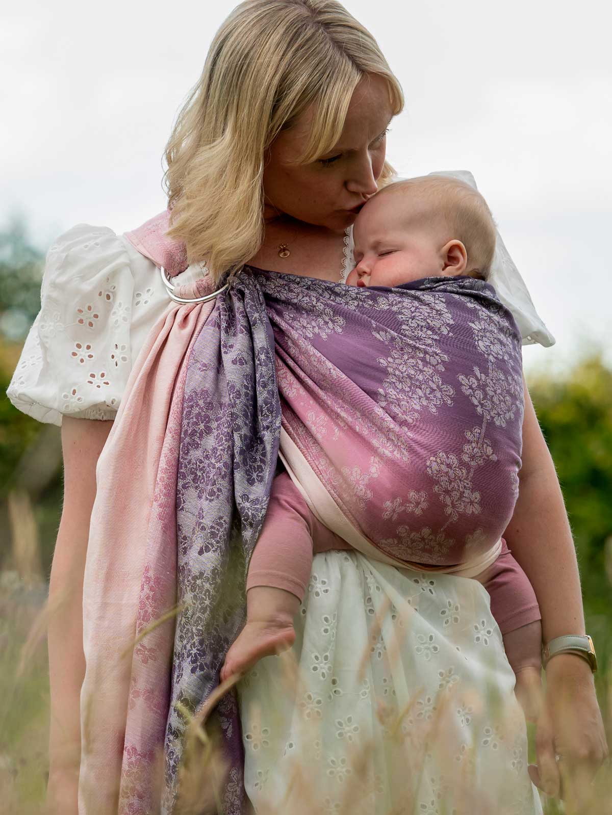 Model carrying baby in blossom patterned ring sling.