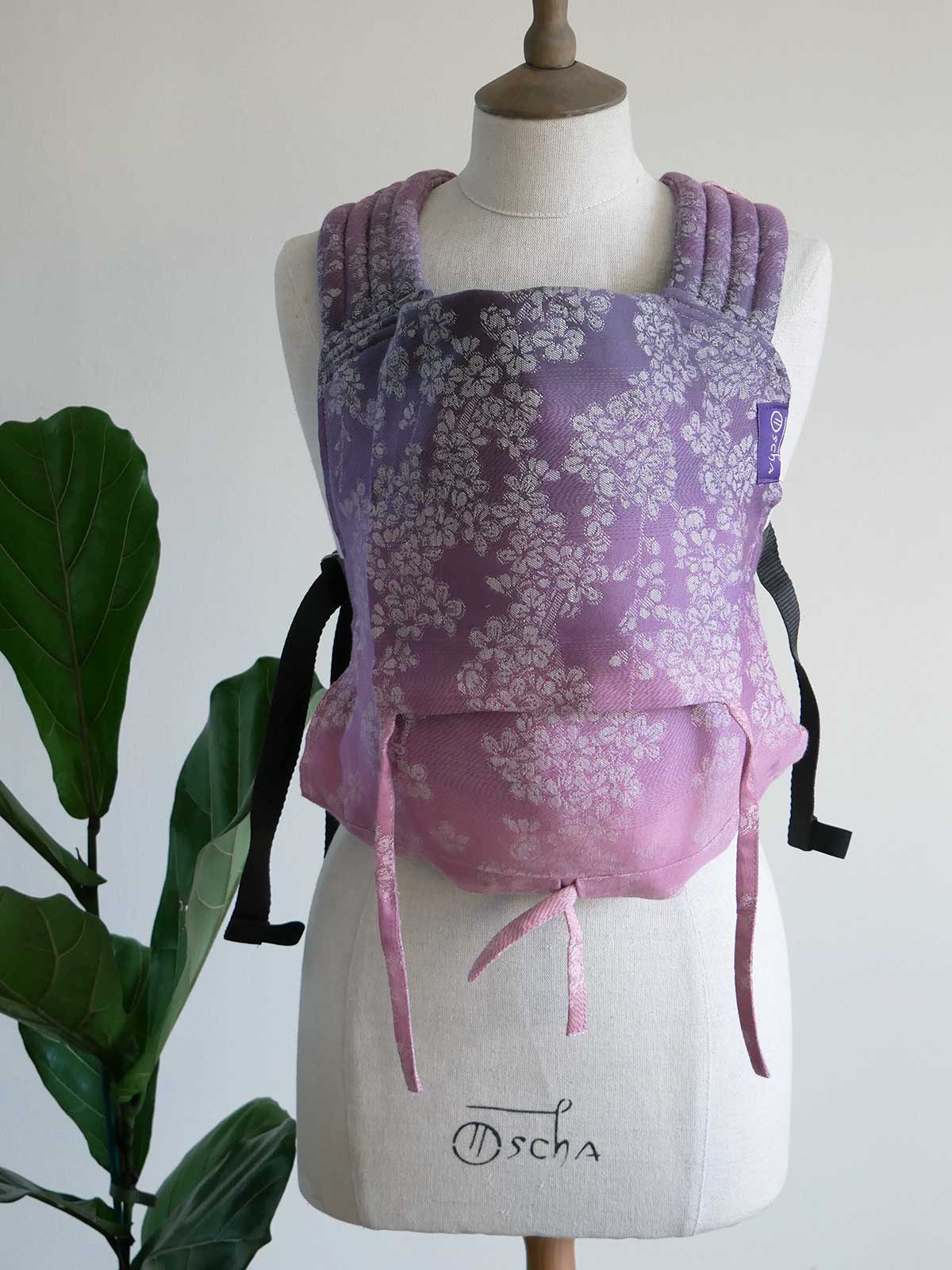 Purple floral baby carrier on a mannequin with a plant in the background