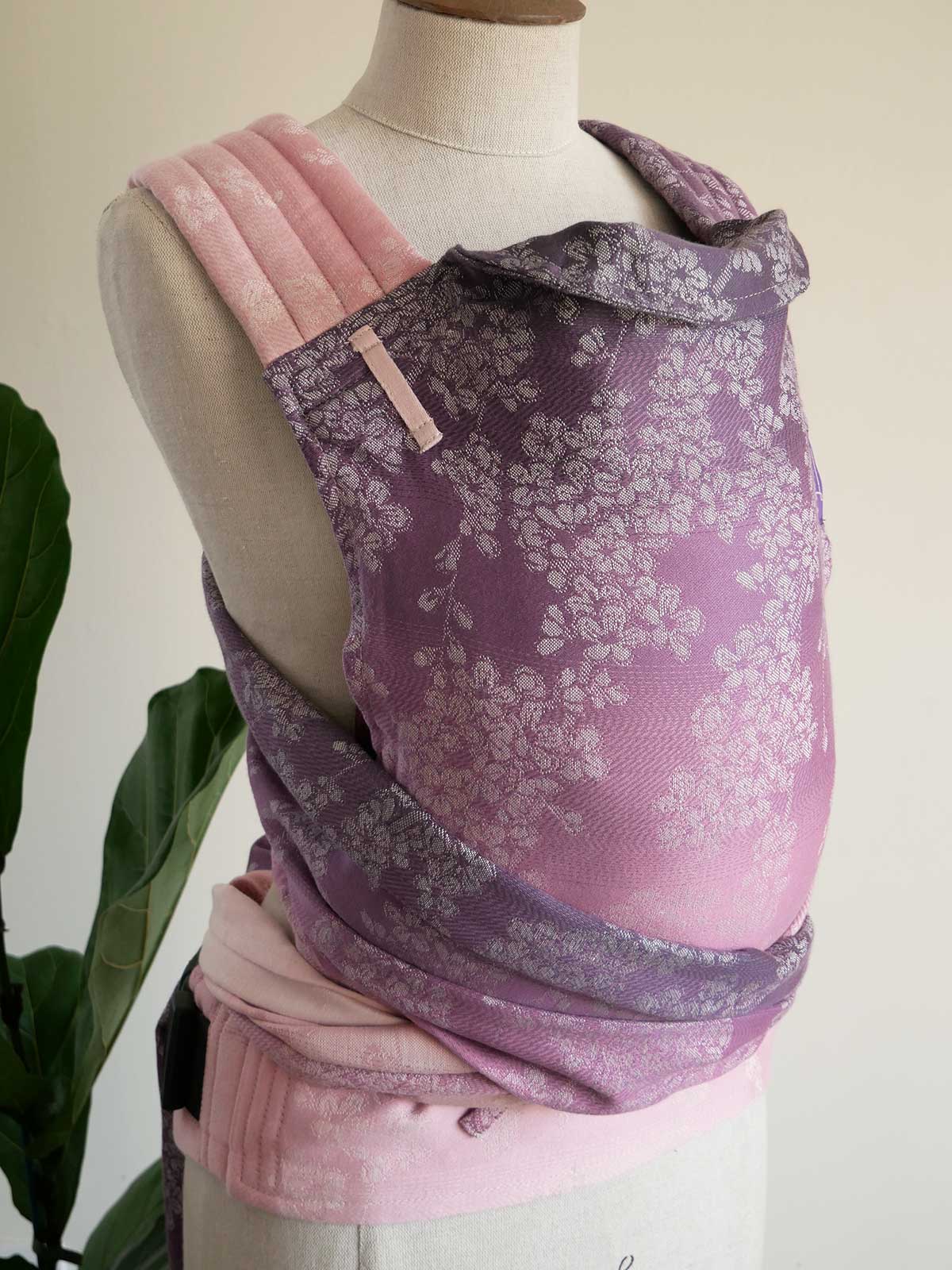 Mannequin wearing a pink and purple floral baby carrier with a plant in the background