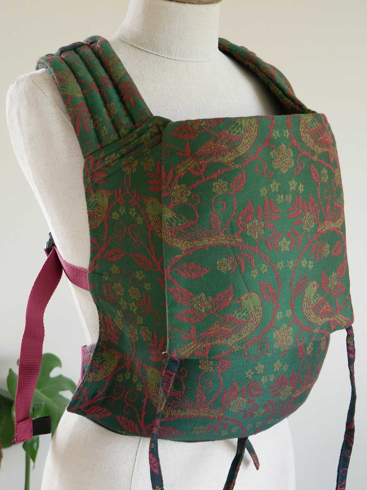 Green and red patterned baby carrier on a mannequin against a white background