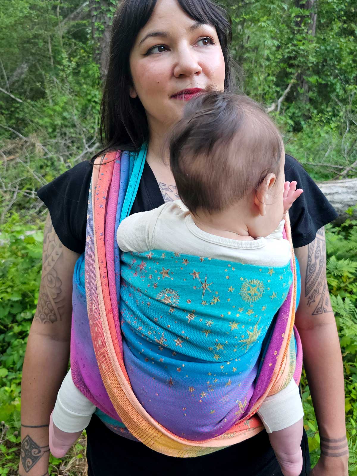 Woman carrying a baby in a colorful woven wrap against a natural background