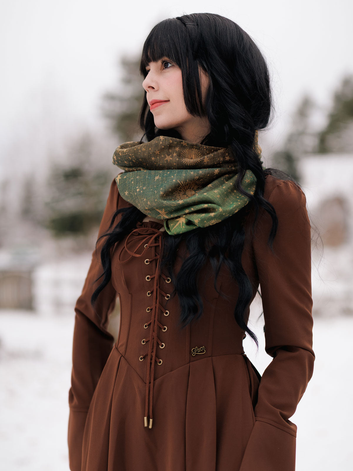 Woman wearing a brown coat and green Constellation Cassiopeia Cowl in a snowy setting