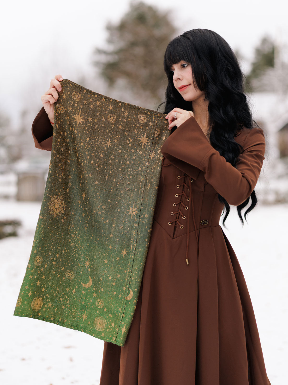 Woman in a brown coat holding a green patterned fabric in a snowy landscape