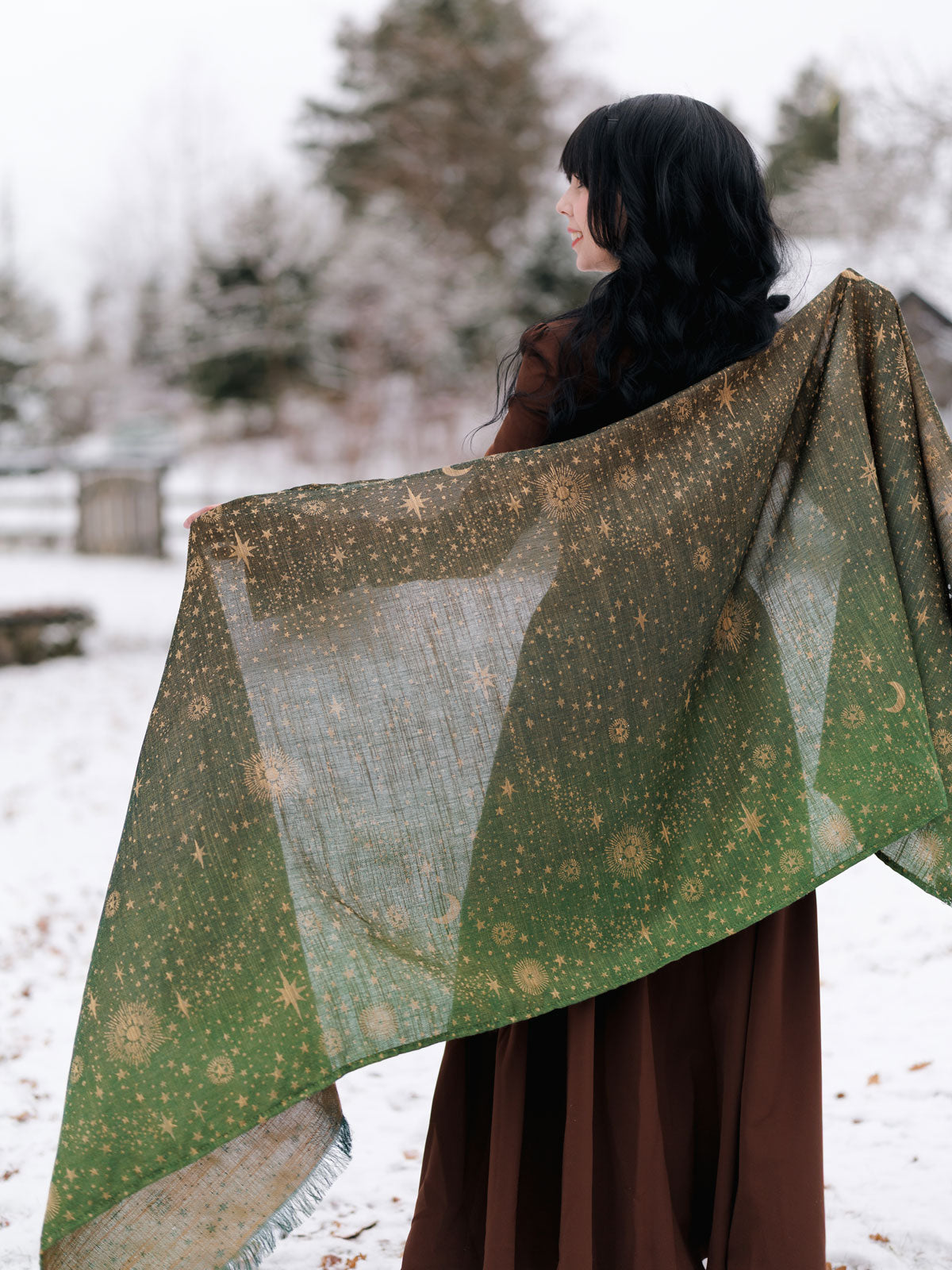 Person holding a large green and gold patterned fabric in a snowy landscape