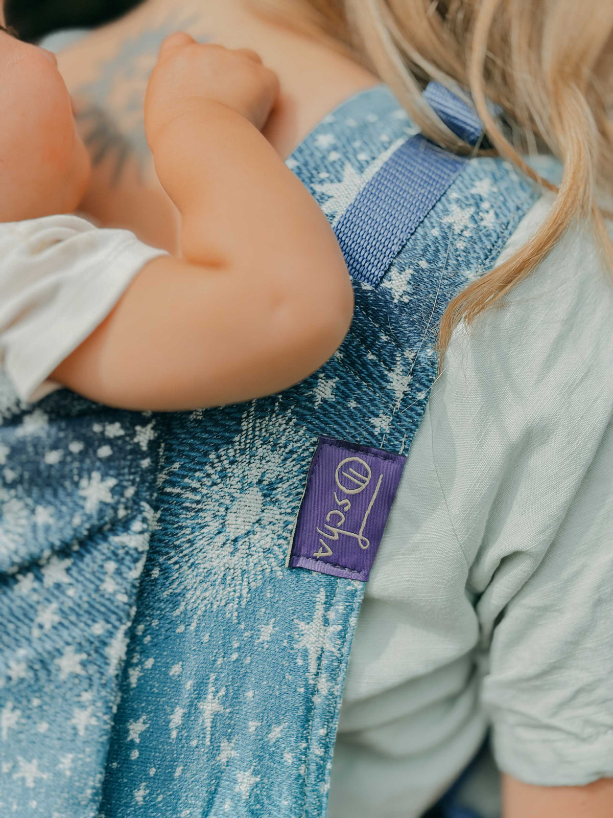 A close up view of Oscha baby carrier with a blue fabric and starry Constellation pattern.