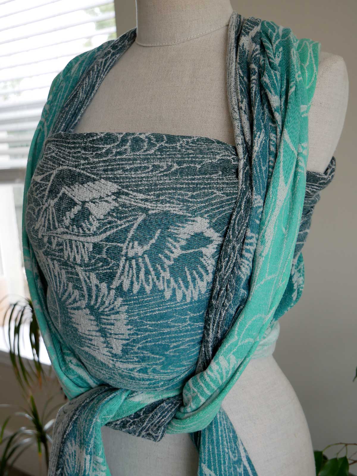 Teal patterned baby wrap on a mannequin against a neutral background