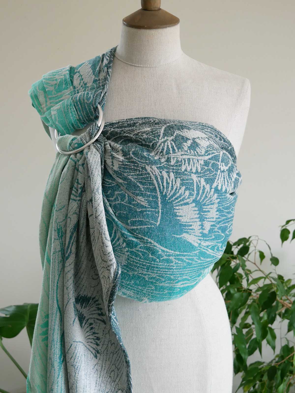Mannequin wearing a teal Cranes Pointbreak Ring Sling with plants in the background