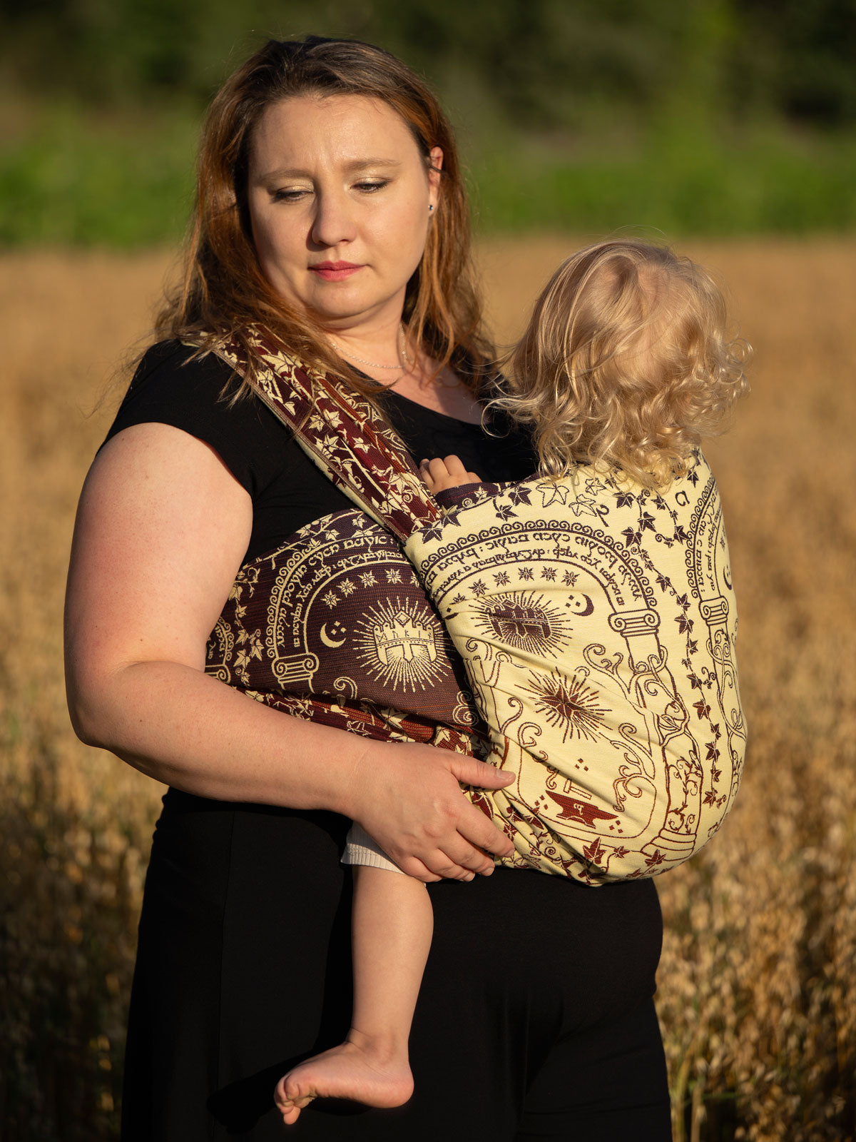 Woman holding a child in a patterned sling against a natural background