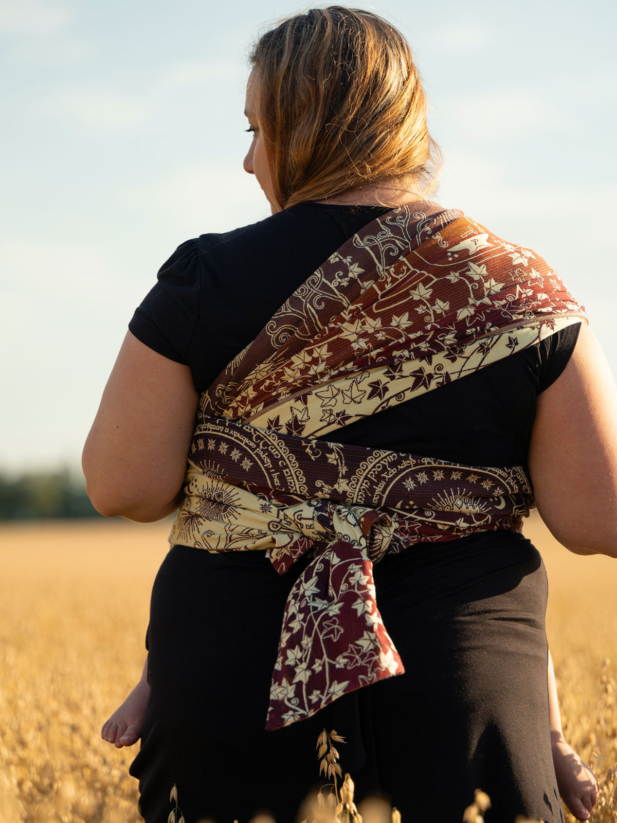 Woman carrying a child on her back with a patterned wrap in a field