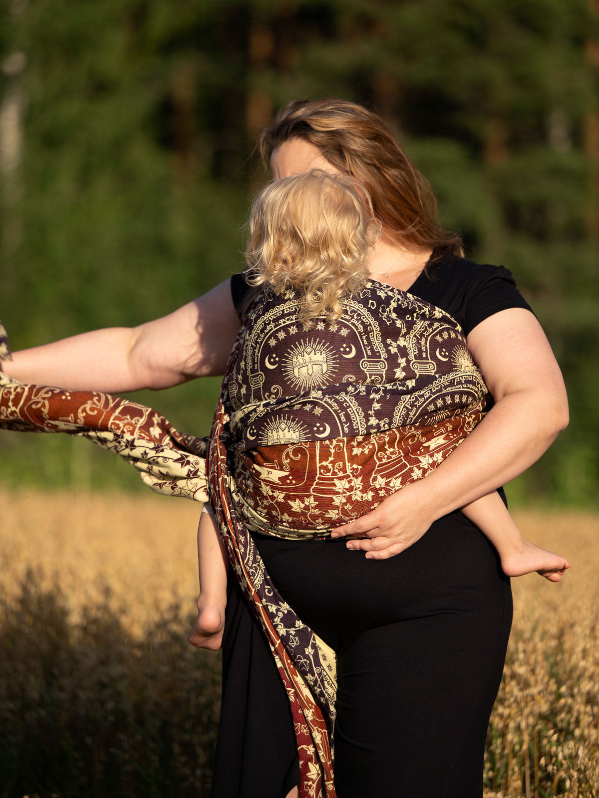 Woman carrying a child in a patterned sling against a natural background