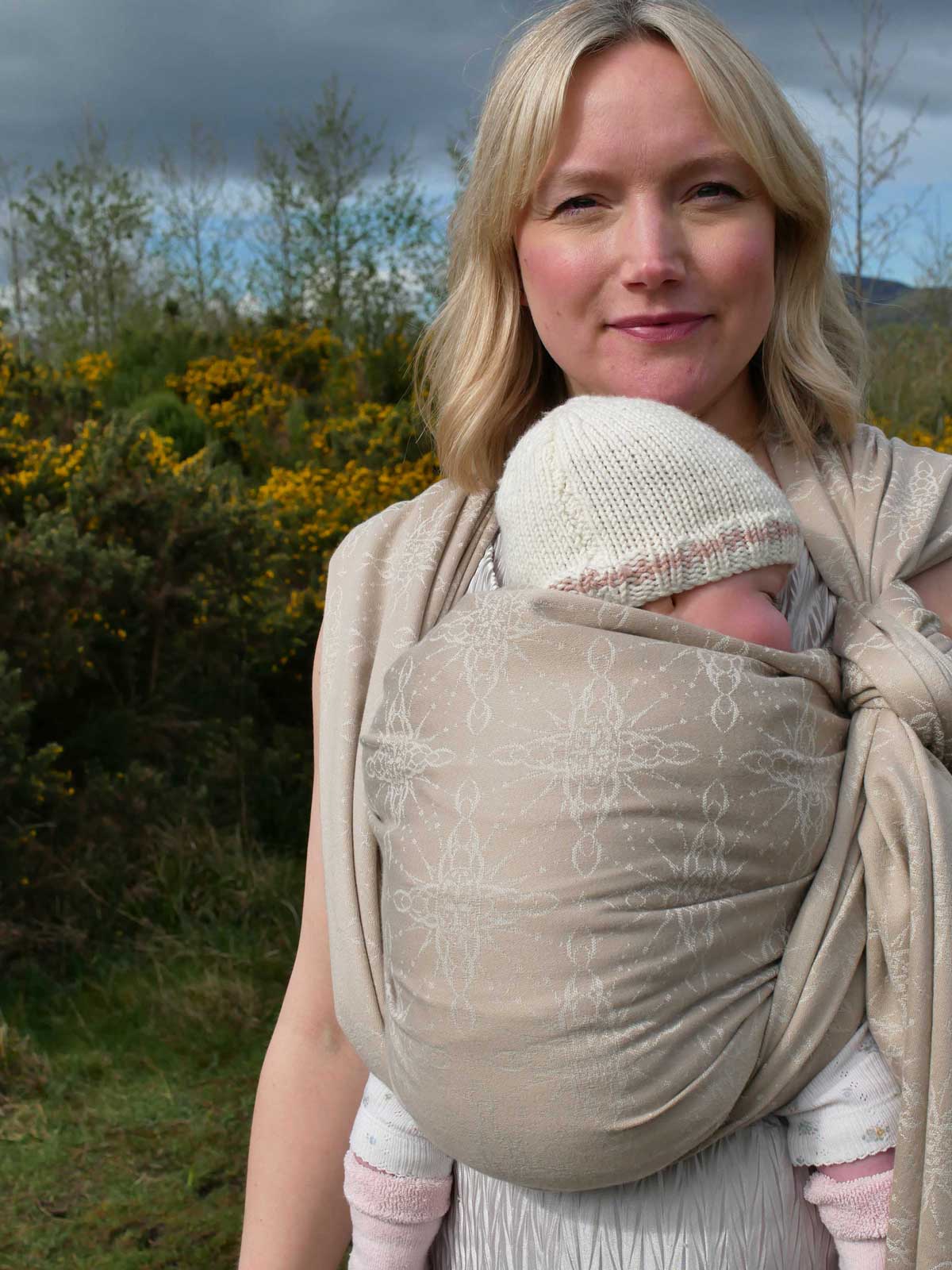 Woman with a baby in a woven wrap with nature in the background