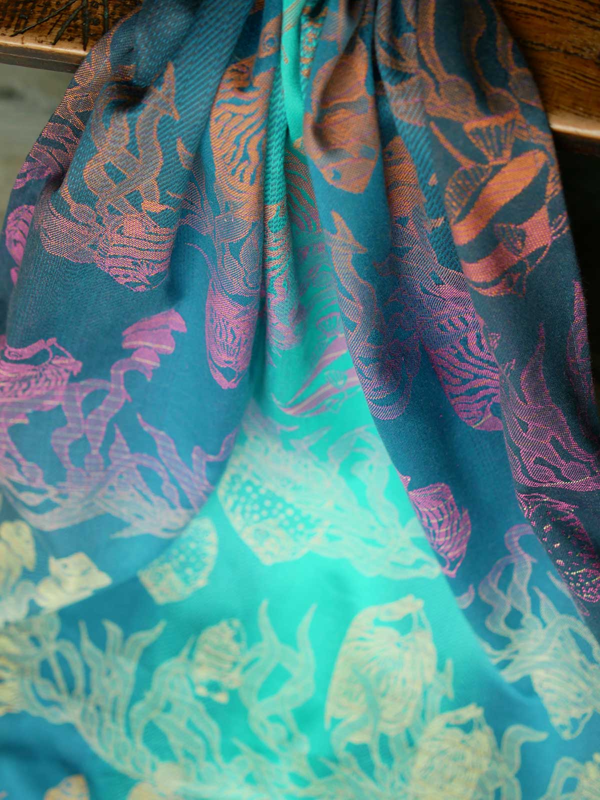 A blue teal woven wrap with tropical fish patten in gold, orange and pink