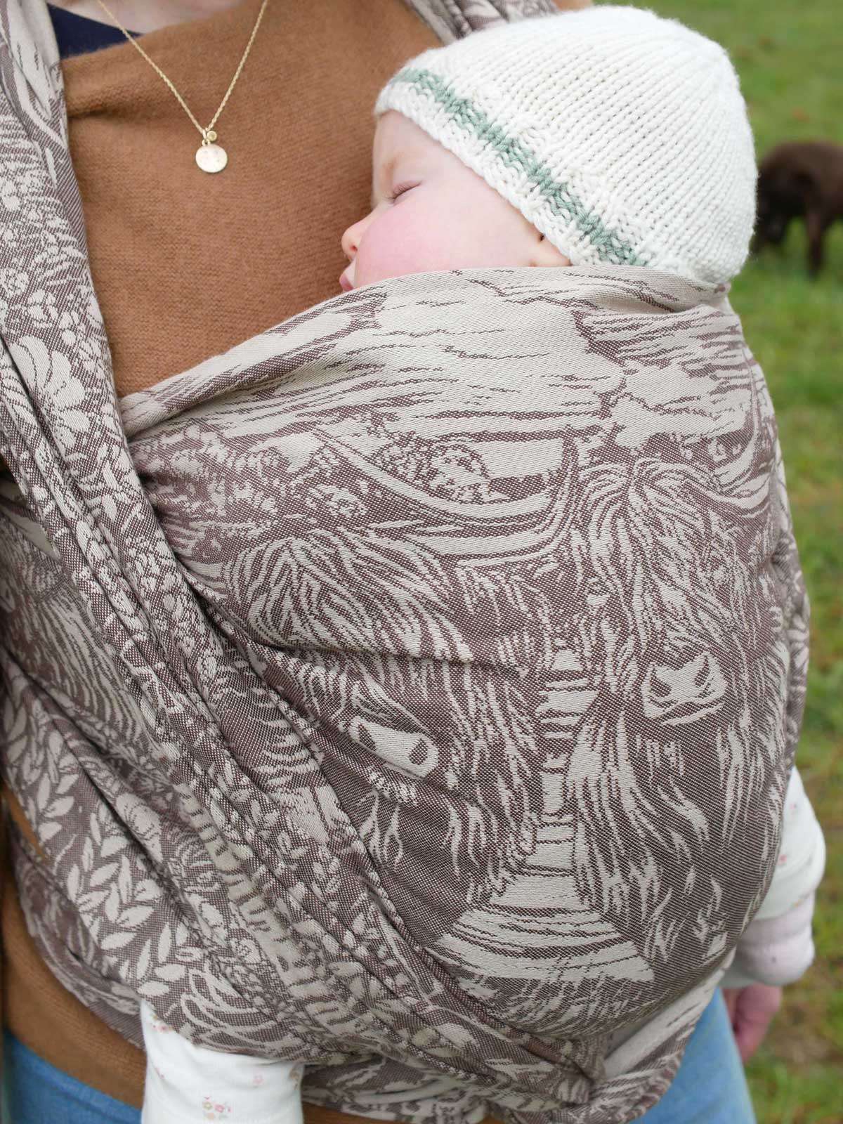 A baby in a woven wrap with a highland cow design.
