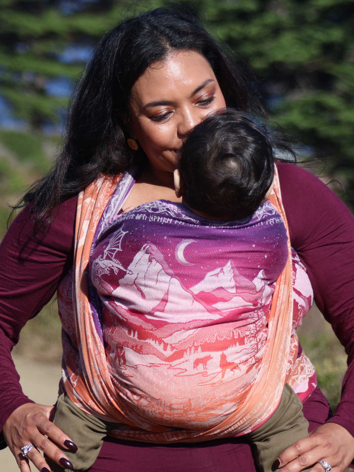Model wearing baby in a The Lord of the Rings design baby wrap. Purple at the top transitions to a warm orange.