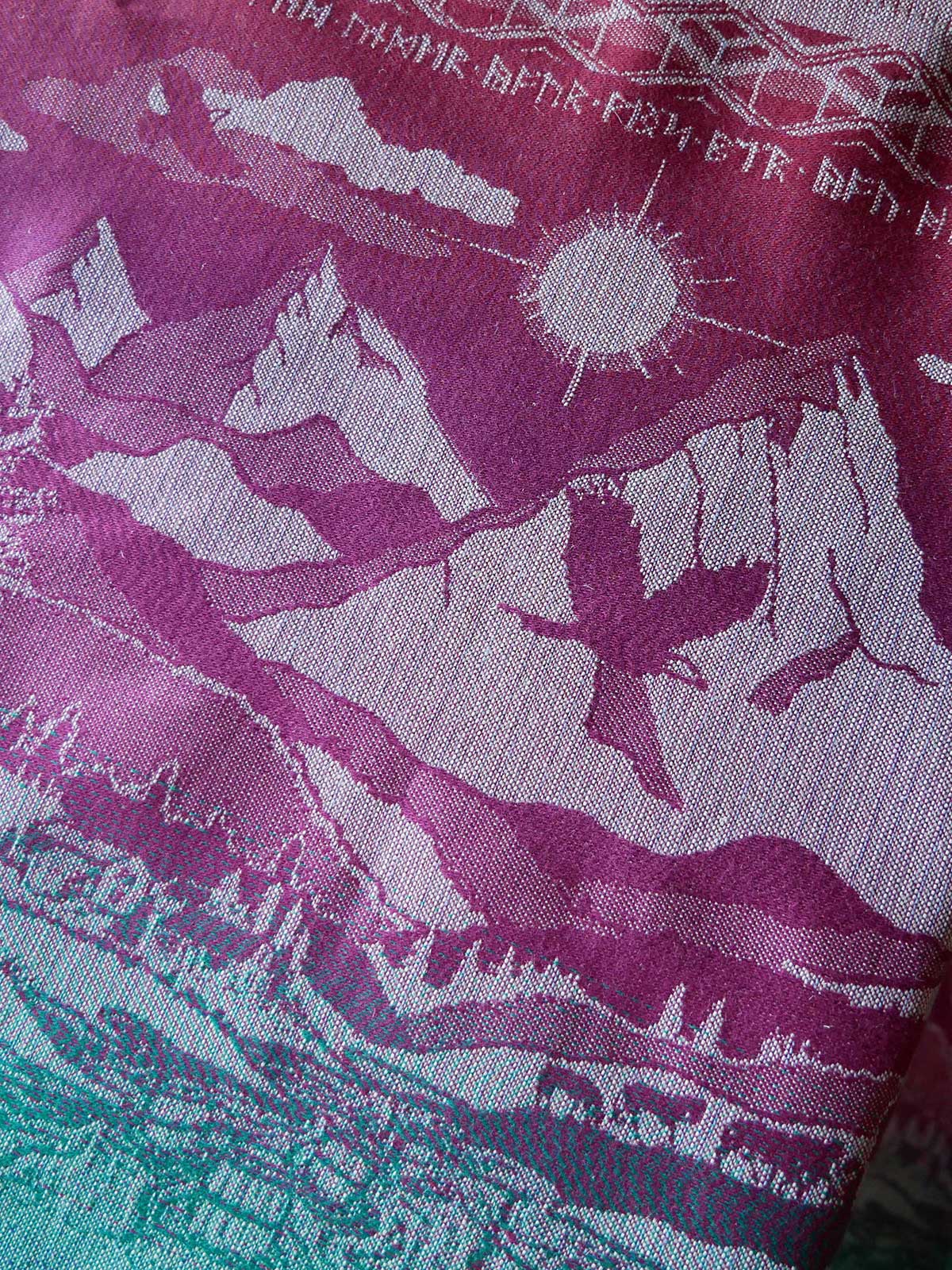 Textile with garnet and green design of mountains, sun, and landscape.