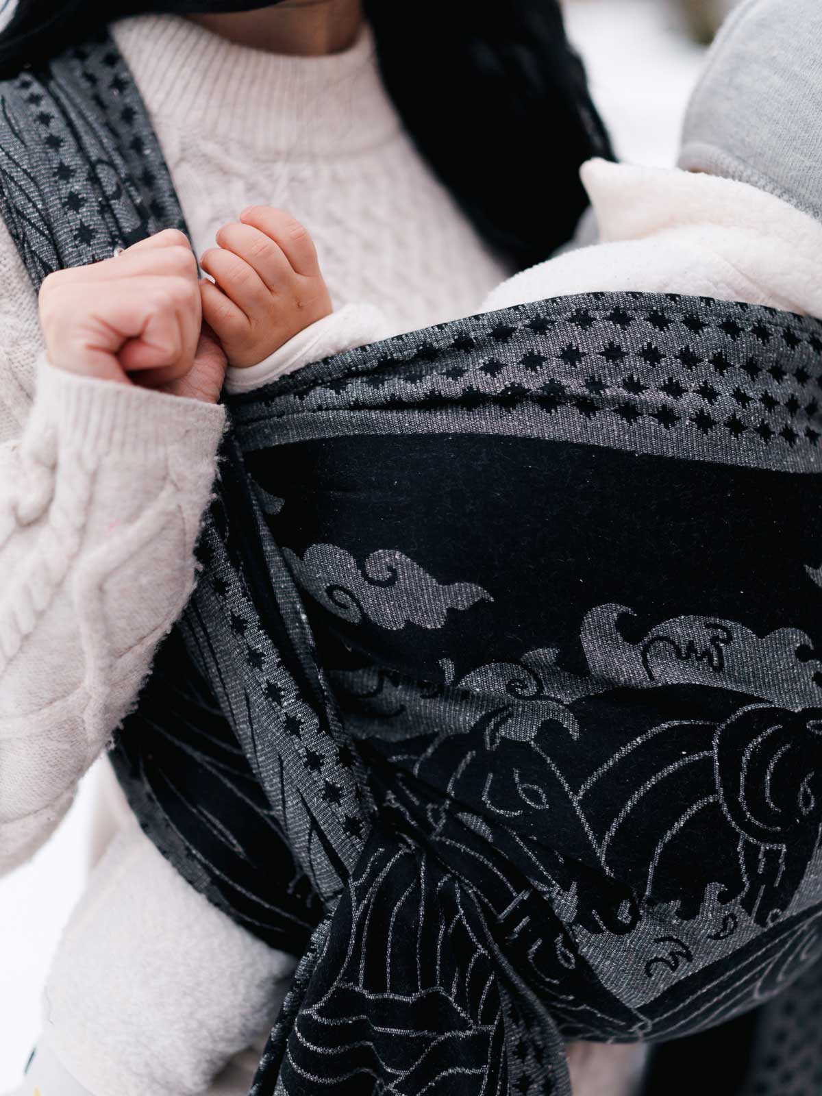 Person wearing a patterned wrap with a baby held close, focusing on the baby's hand.