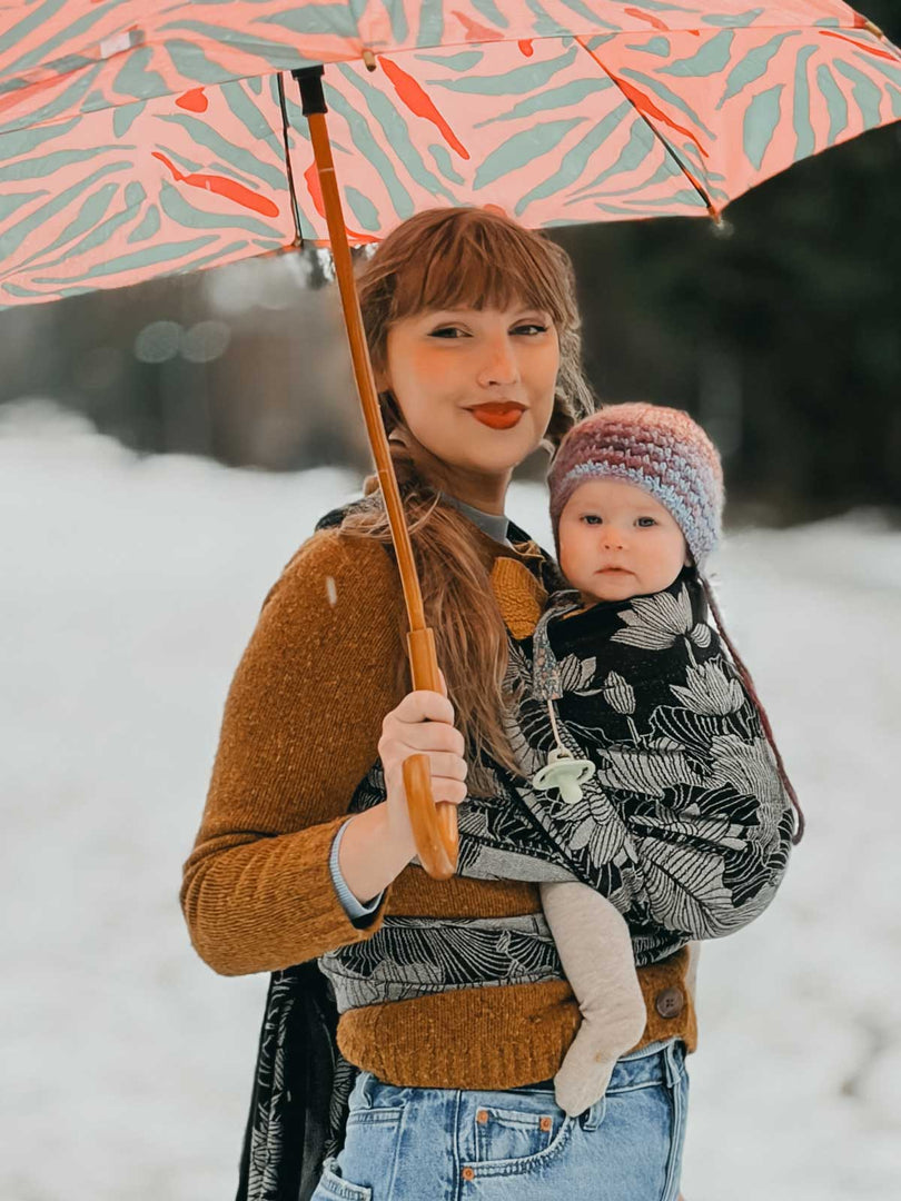 Woman carrying a baby in a woven wrap and an umbrella in a snowy setting