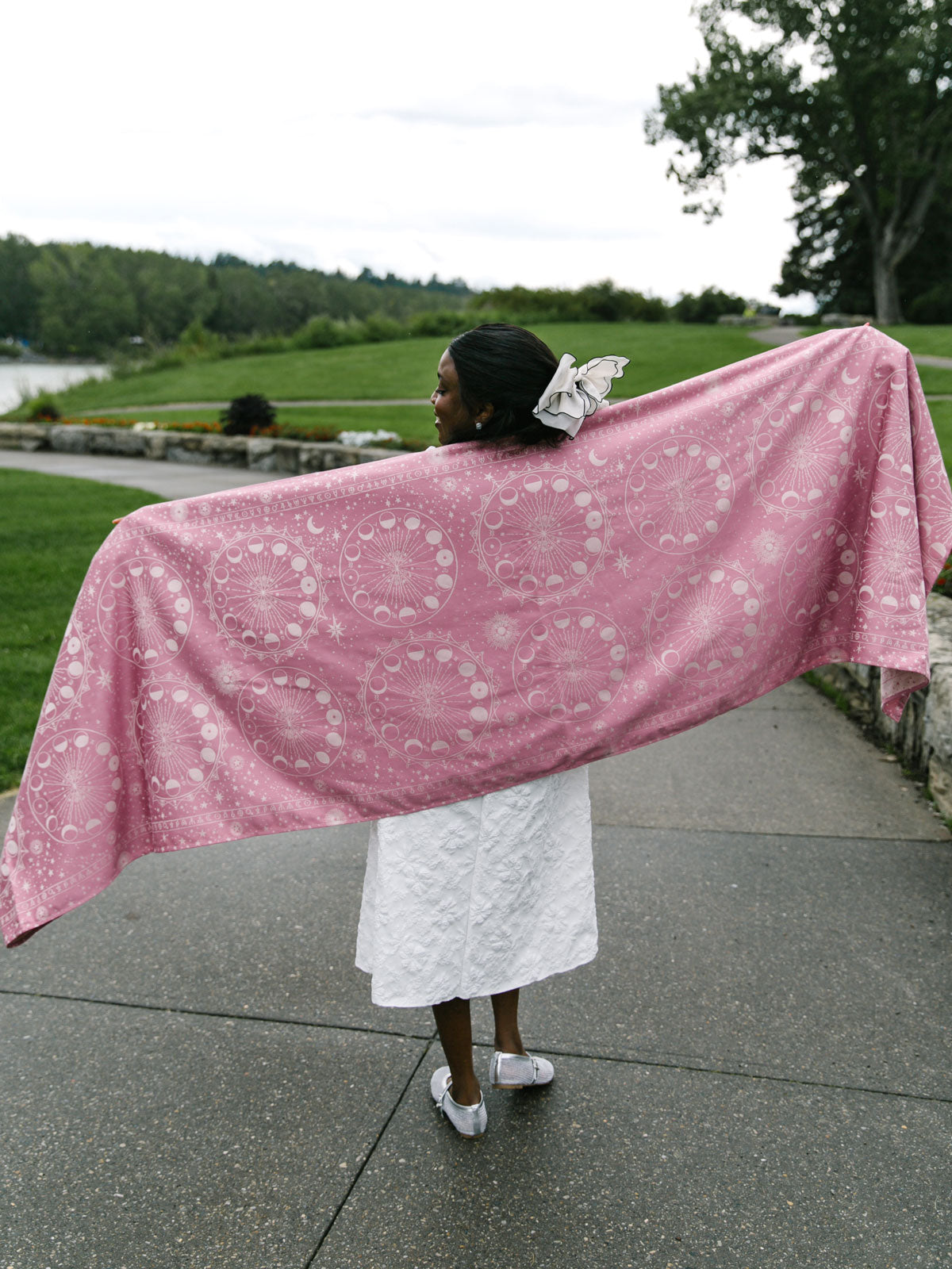 Person holding a pink patterned woven wrap outdoors on a path with greenery.