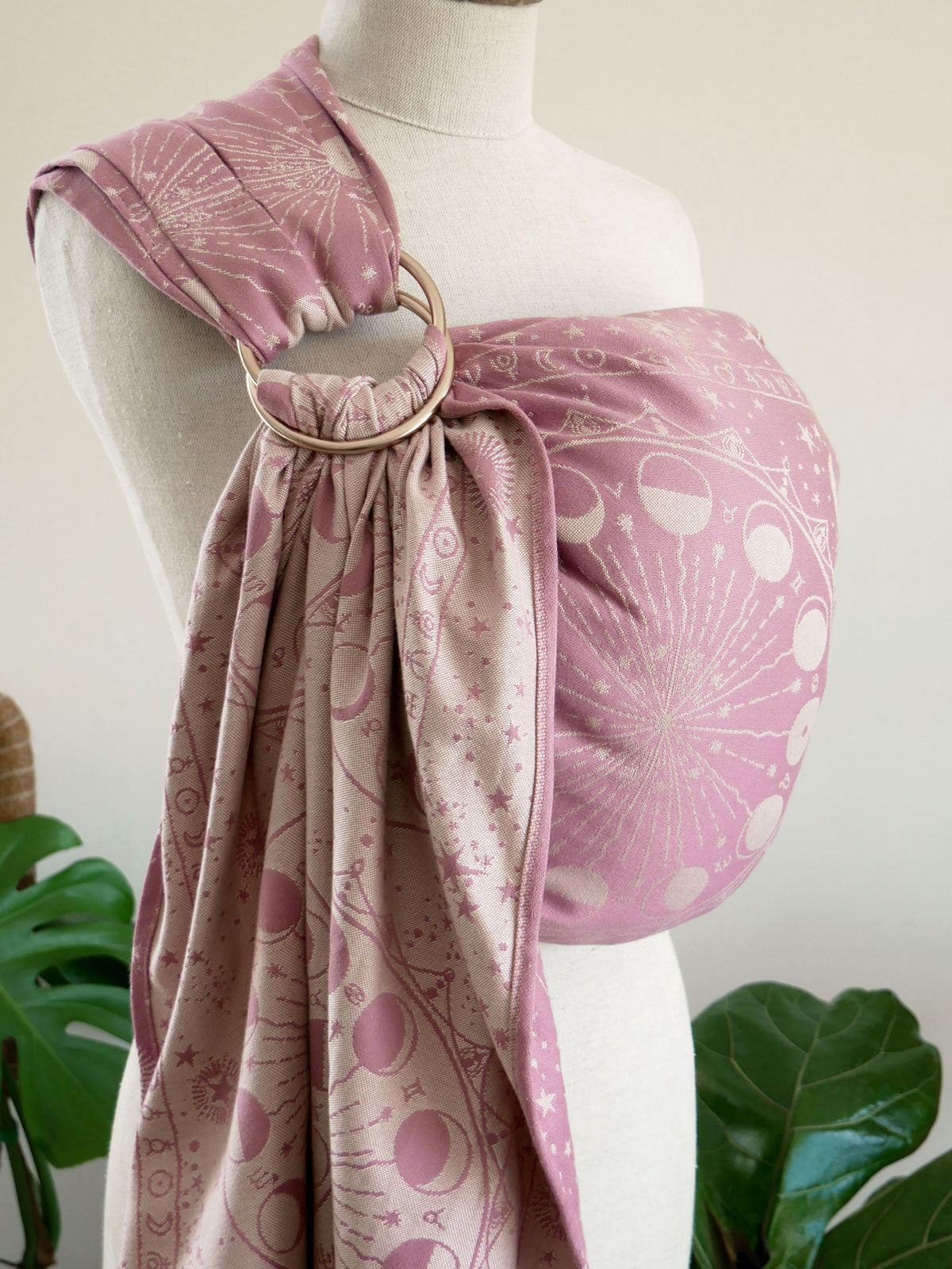 Mannequin wearing a pink ring sling, surrounded by green plants.