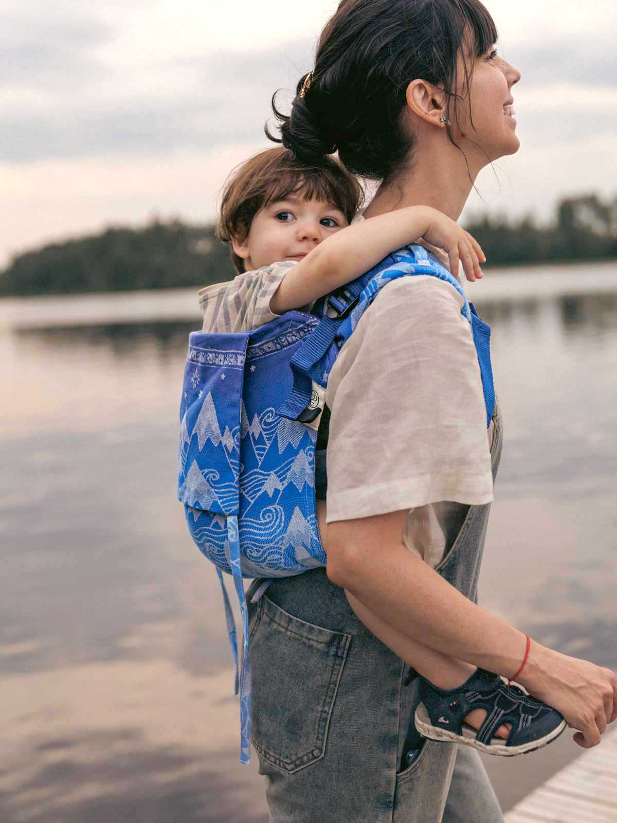 Side view of a child in a blue Onbuhimo with mountain pattern on a woman's back.