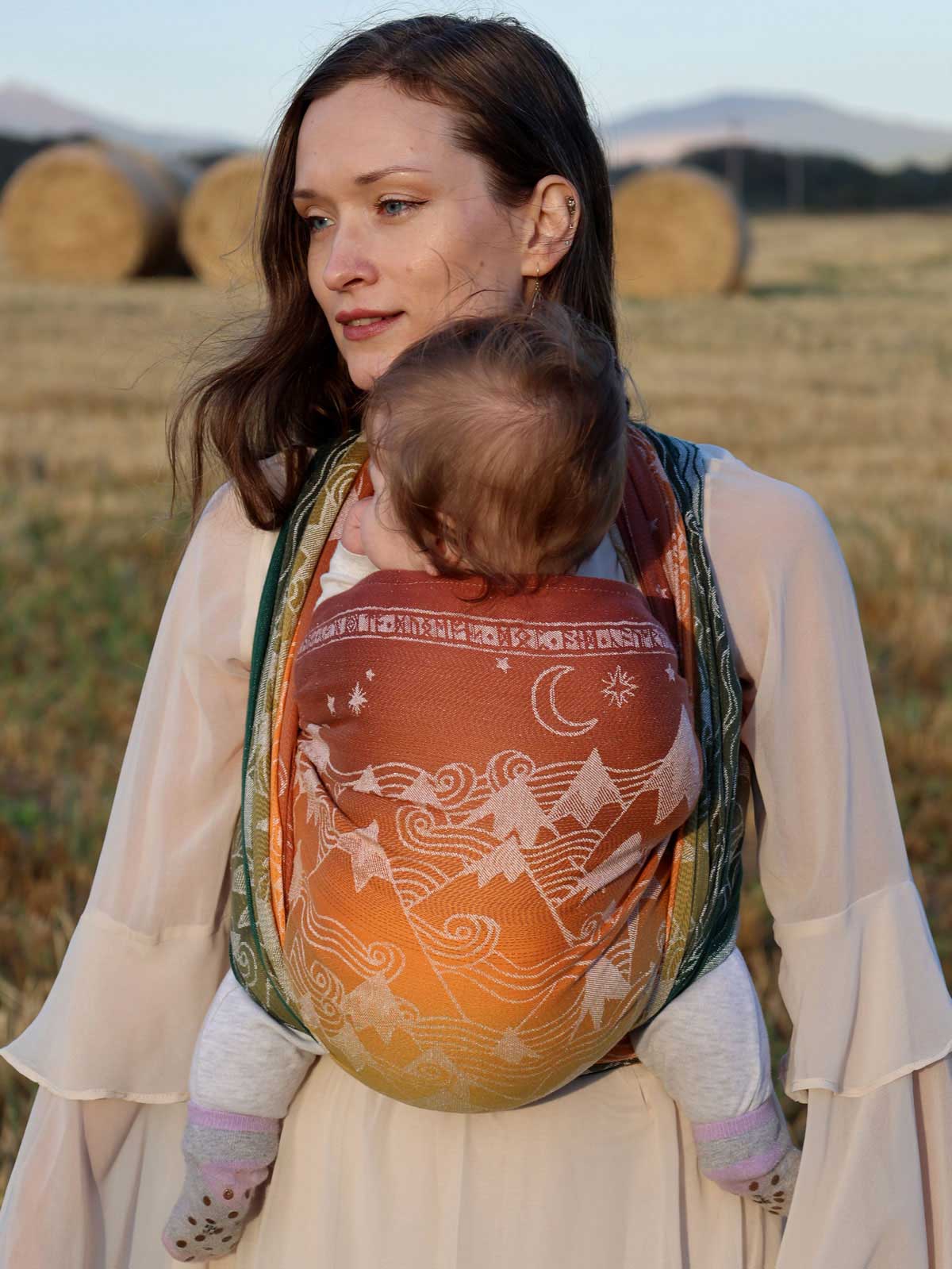 Woman carrying a baby in Misty Mountains Summit Ember Baby Wrap with a scenic background