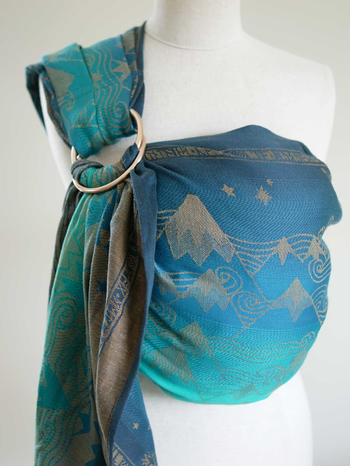 A blue teal ring sling with a gold mountain pattern on a mannequin