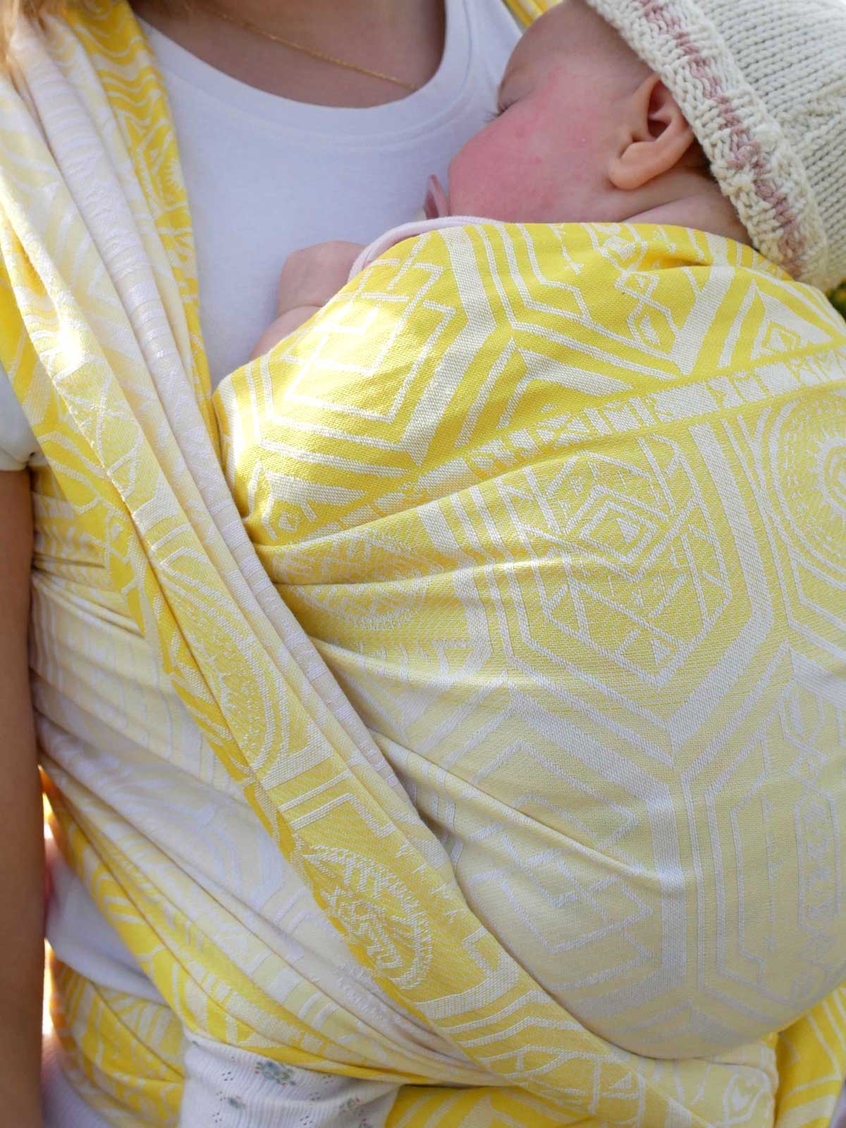 Close up of a baby in a yellow woven wrap with geometric pattern
