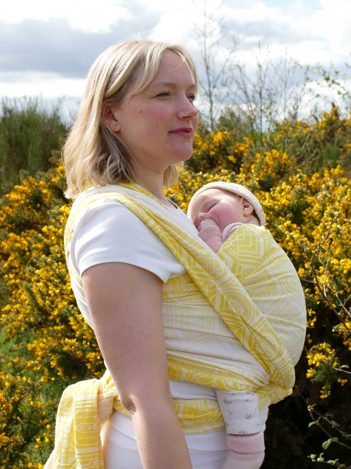 Woman wearing a baby in a yellow woven wrap with geometric pattern