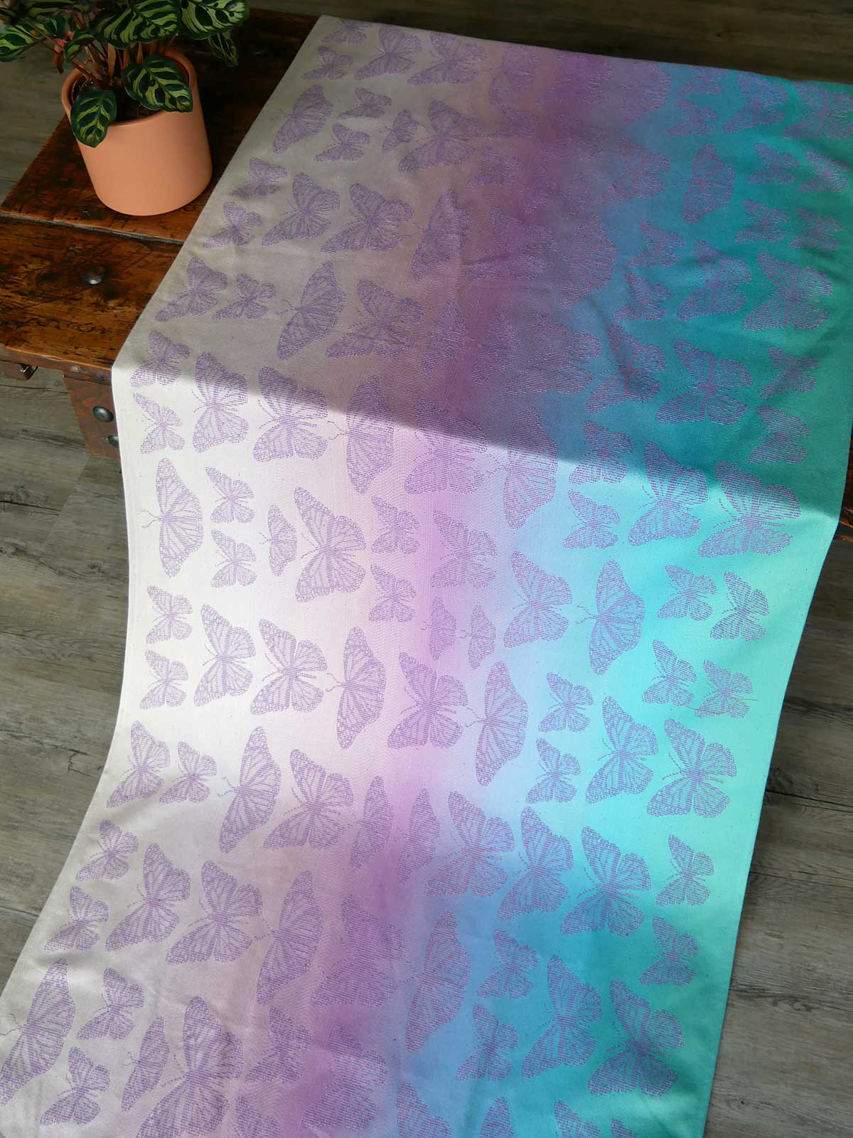Butterfly-patterned fabric with a gradient of purple to green on a wooden surface.