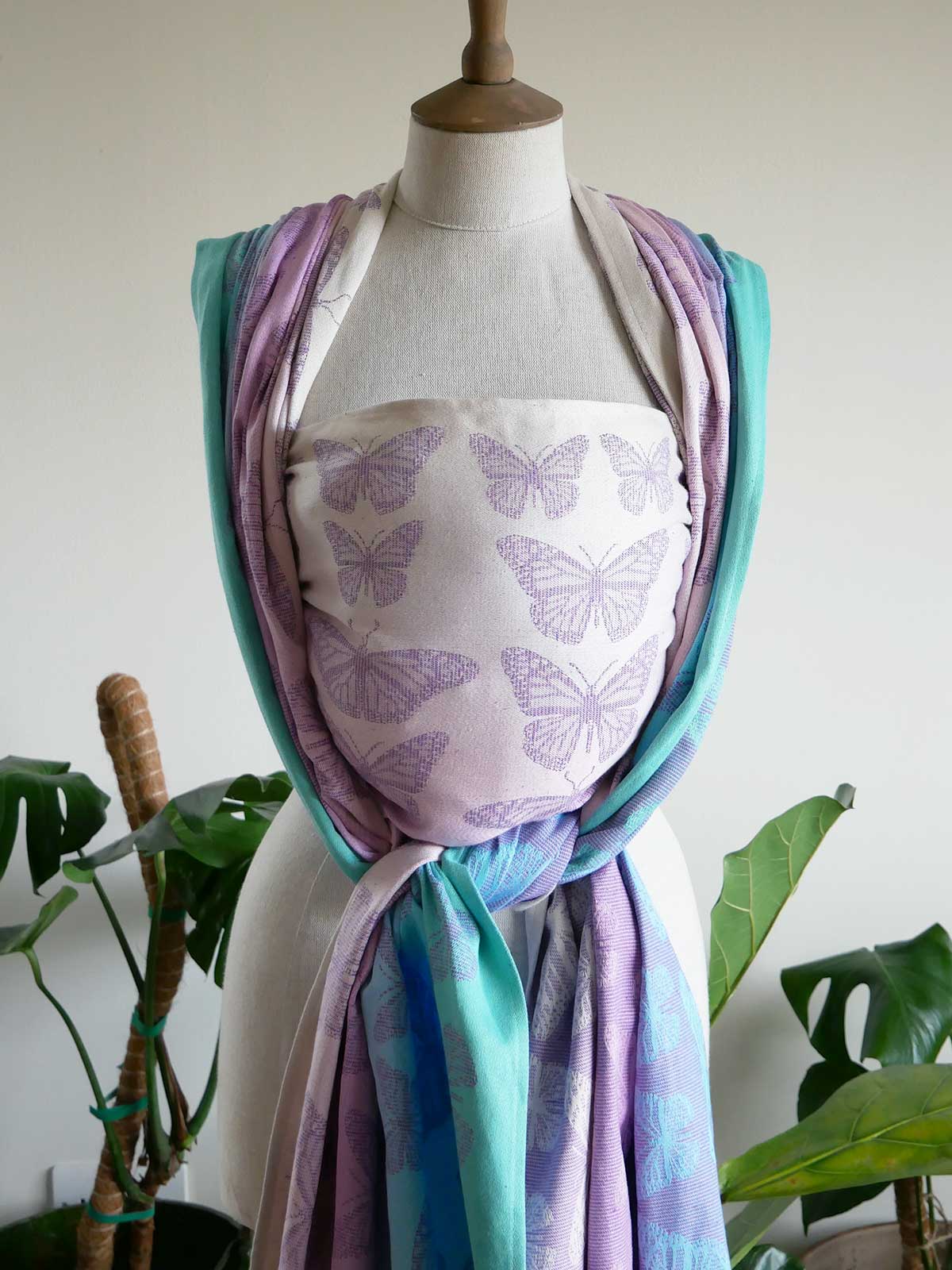 Mannequin wearing a colorful woven wrap with butterfly patterns in a home setting.
