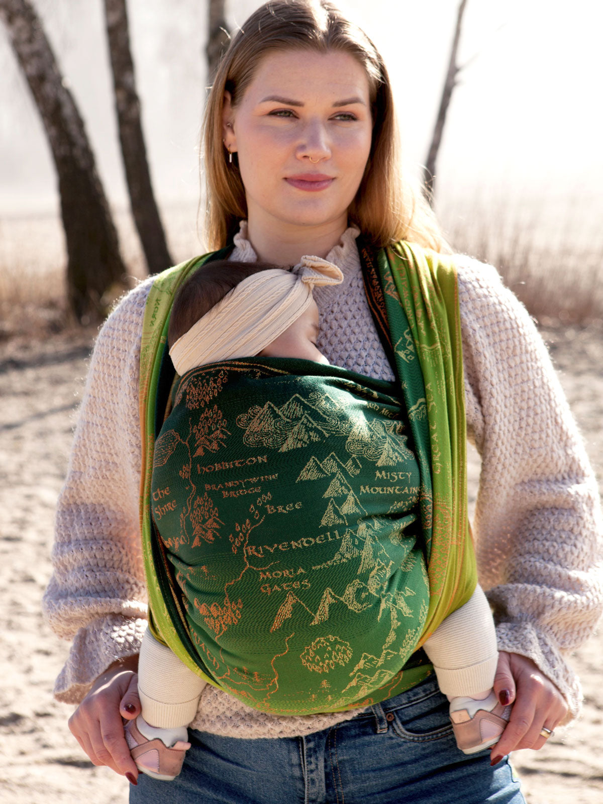 Woman carrying a baby in a green woven wrap with map design.