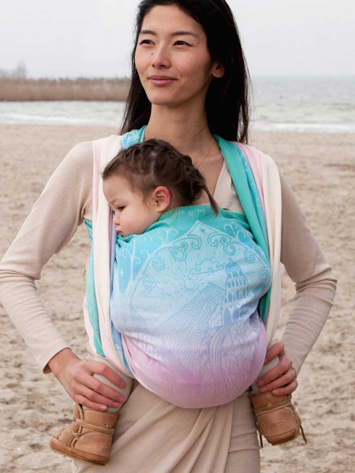 Woman carrying a child in a baby carrier on a beach