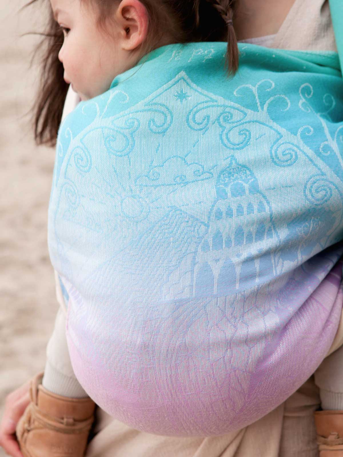 Child being carried in a pastel coloured sling with intricate patterns.