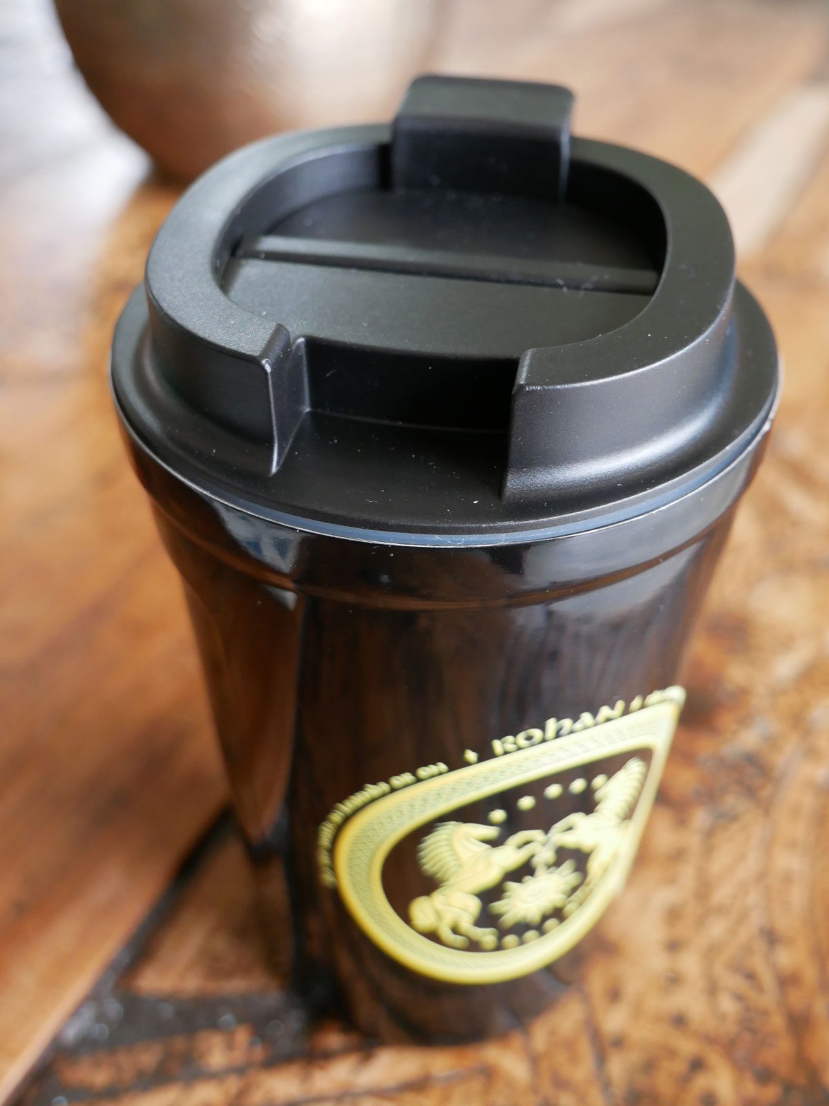 Black coffee cup with a gold emblem on a wooden surface