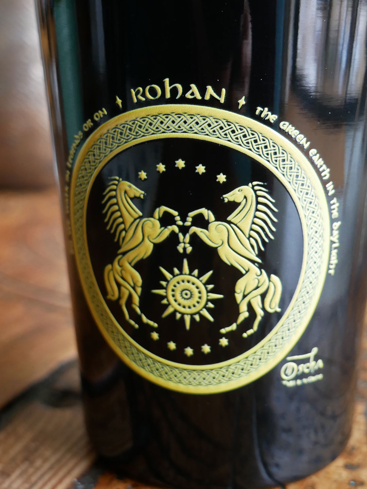 Travel mug with a decorative label featuring two horses and the word 'Rohan' on a wooden surface.