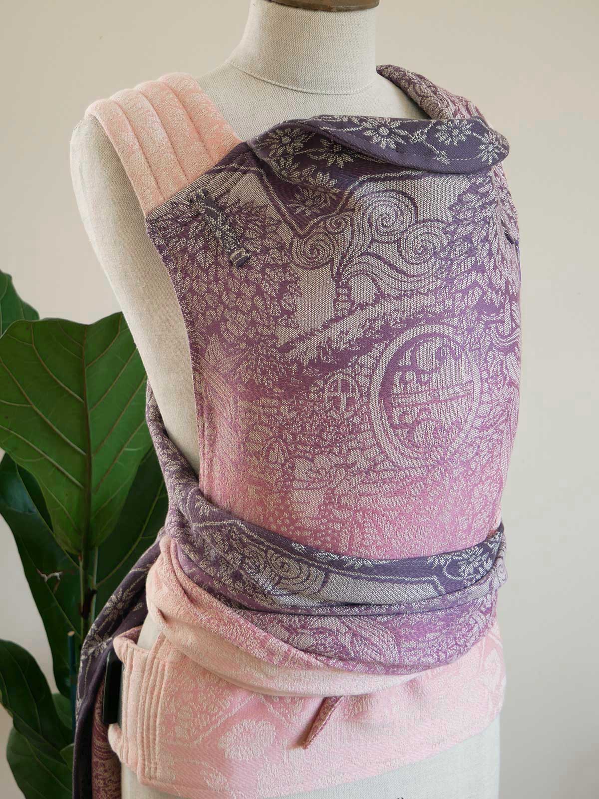 Mannequin wearing a patterned baby carrier with pink accents against a neutral background