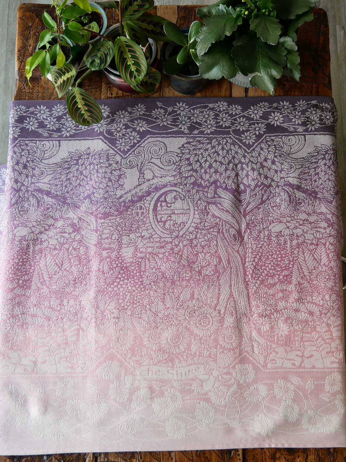 Decorative fabric with intricate patterns on a wooden surface with plants.