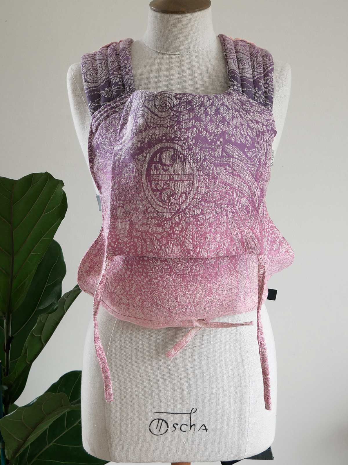 Pink baby carrier with intricate patterns on a mannequin against a white background