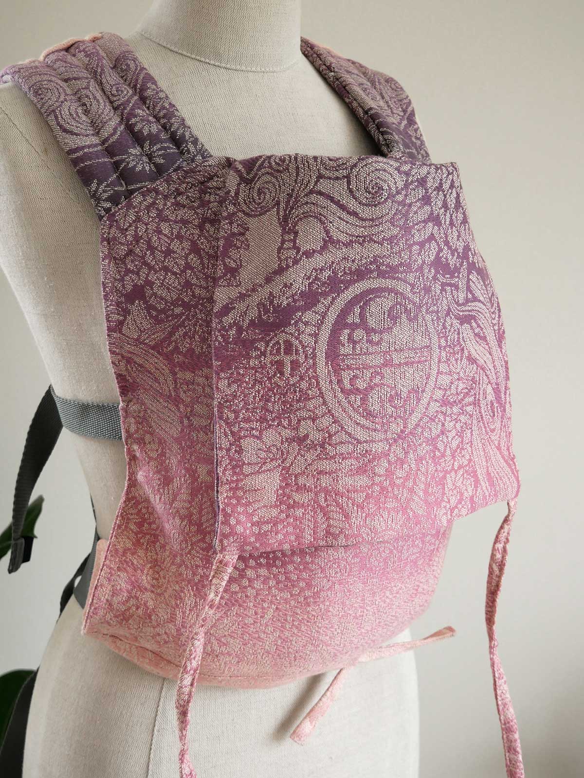 Pink and purple patterned baby carrier on a mannequin against a neutral background