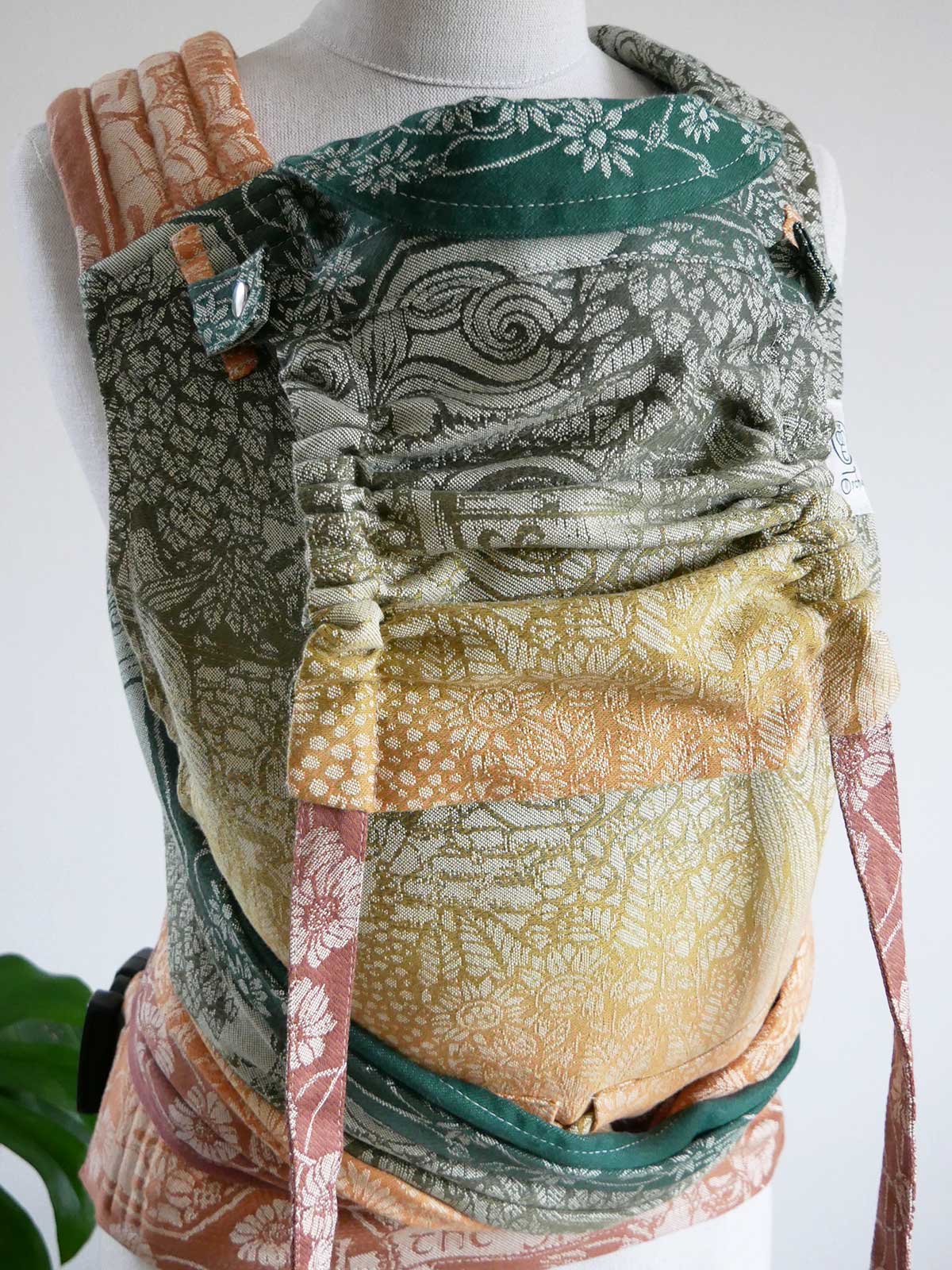 Autumnal coloured Shire Harvest Light Cairis Baby Carrier on a mannequin with a white background