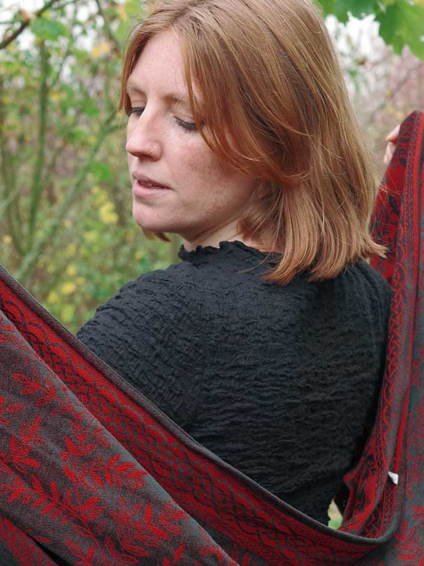 Woman wearing a red and black patterned shawl in a forest setting