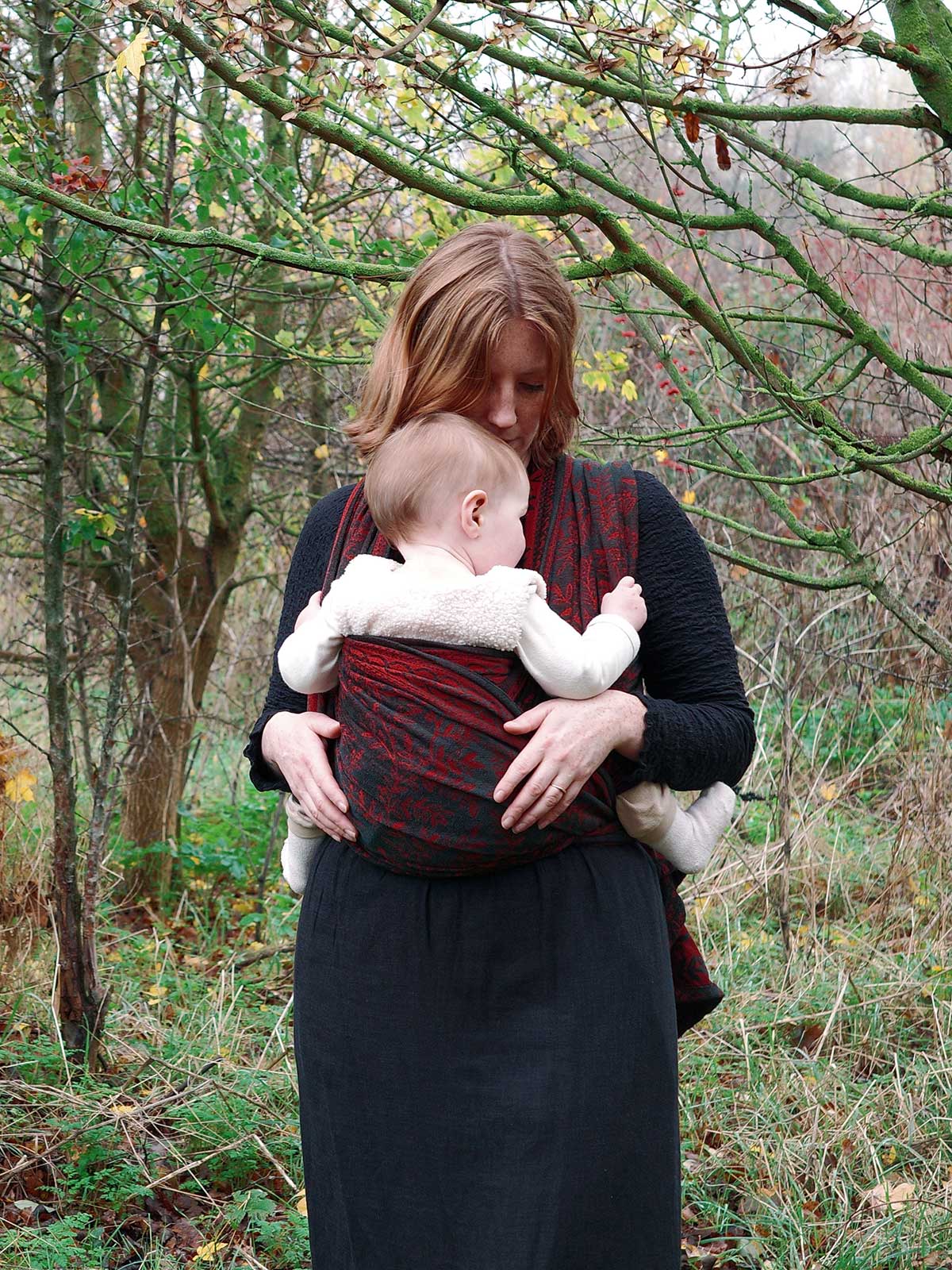 Woman holding a baby in a sling amidst trees and foliage