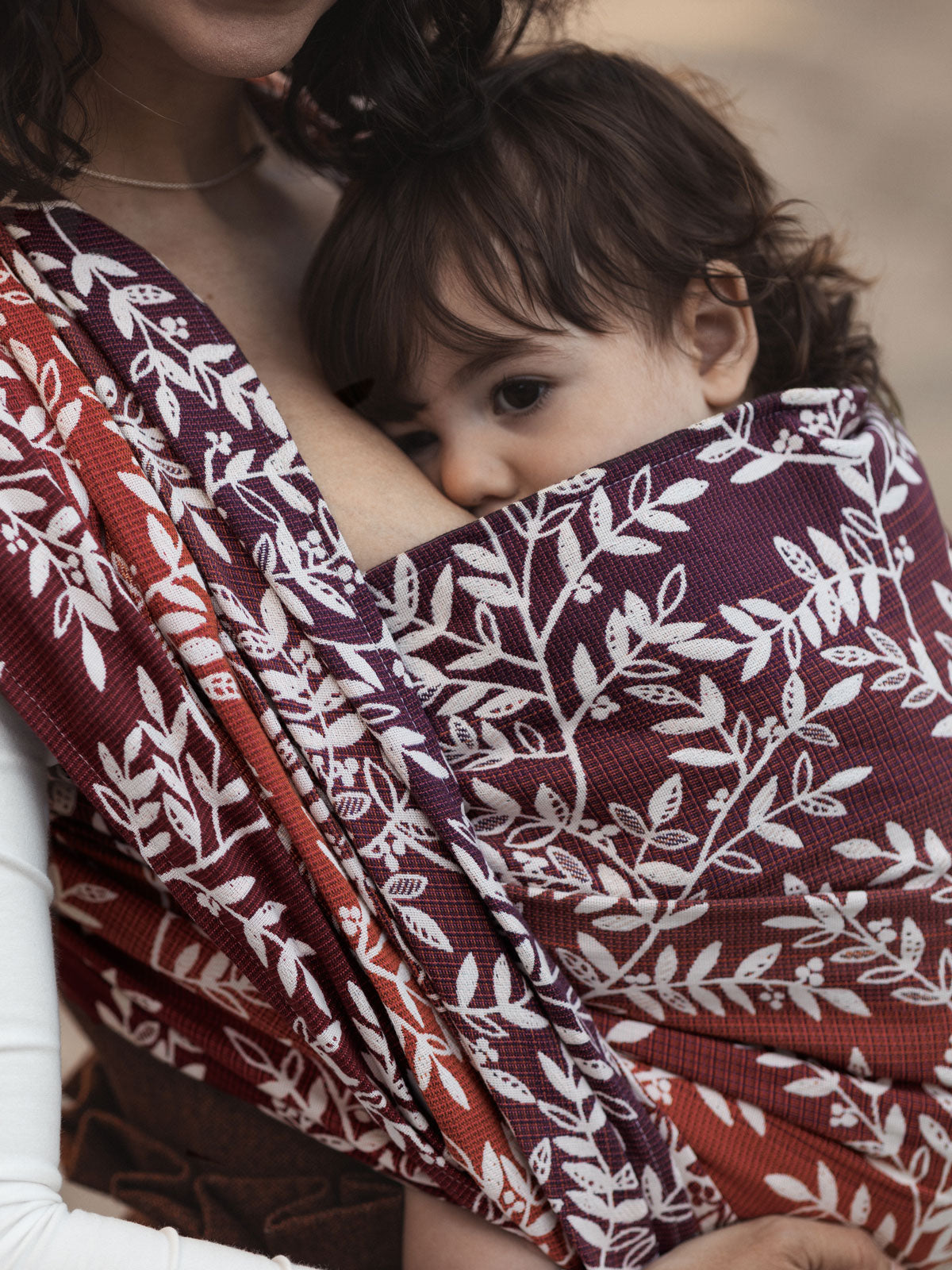Person holding a child wrapped in a woven wrap sling with willow leaf designs.