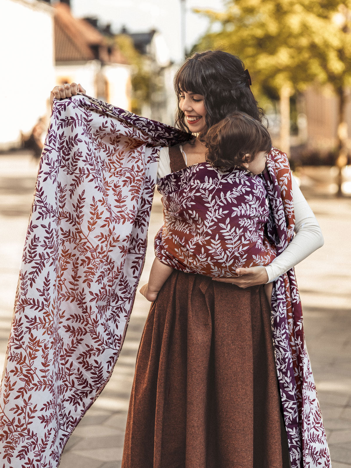 Woman holding a baby in a sling with a floral patterned wrap outdoors.