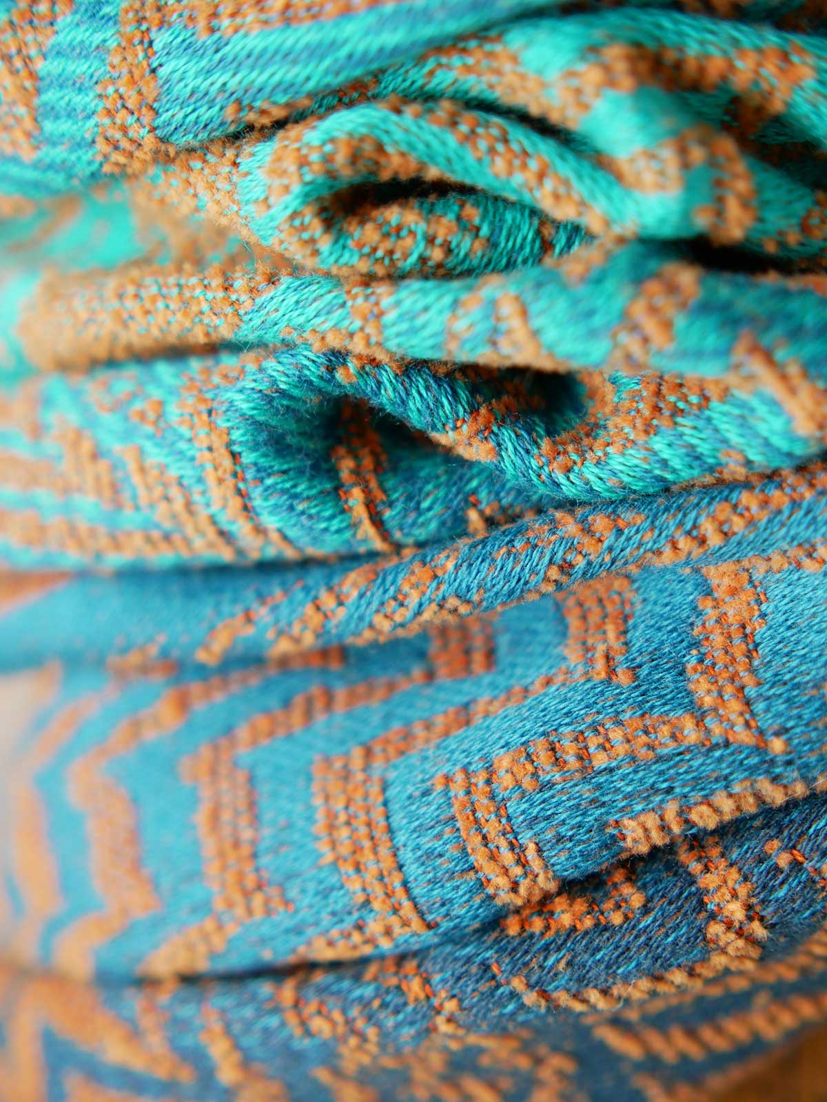 Close up of fox pattern on teal and rust colour baby wrap fabric.