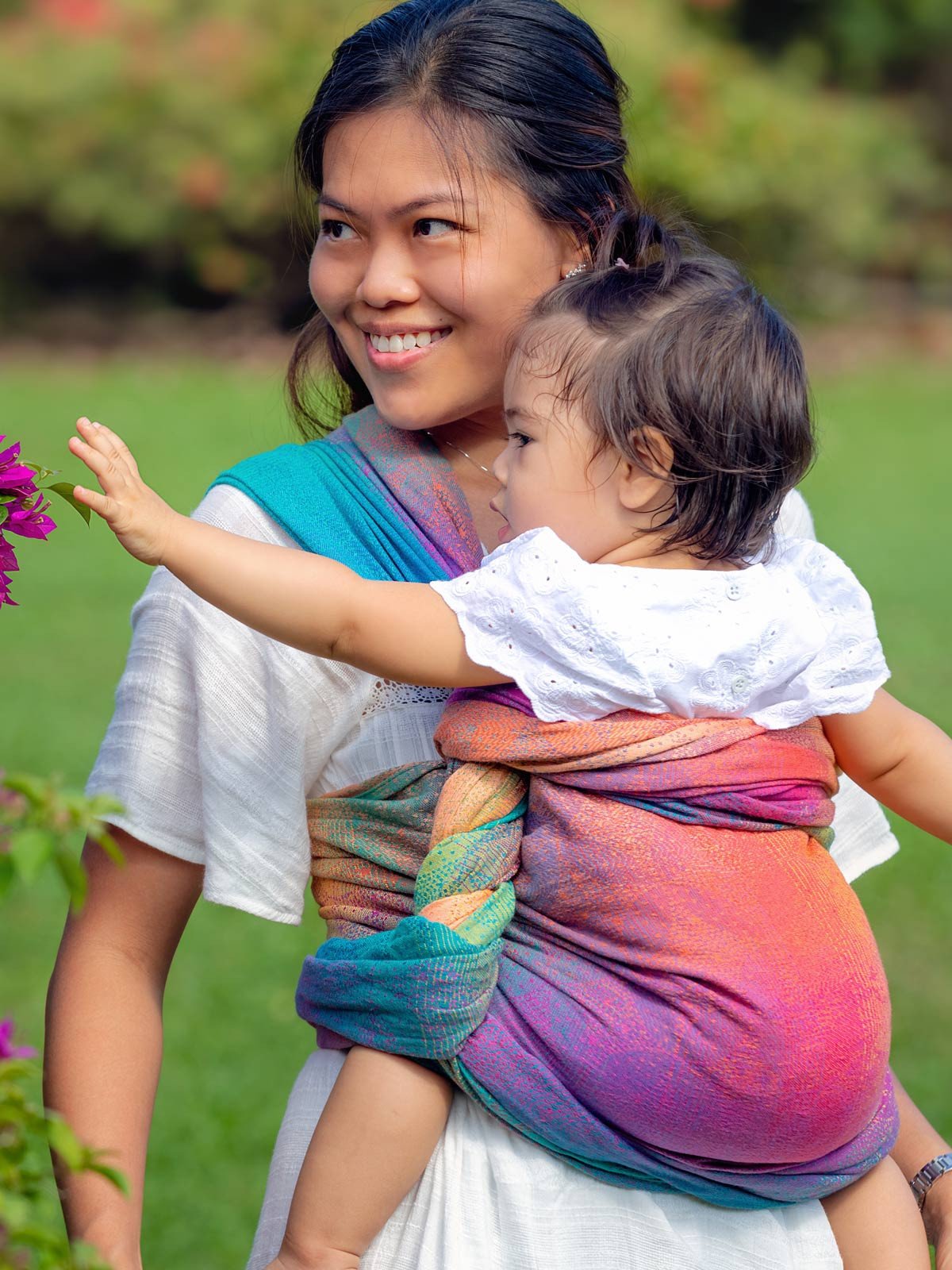 A person holding a child wrapped in a multicolored baby wrap with a starry night design.