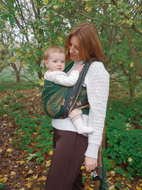 Woman carrying a baby in a sling outdoors in a forest setting