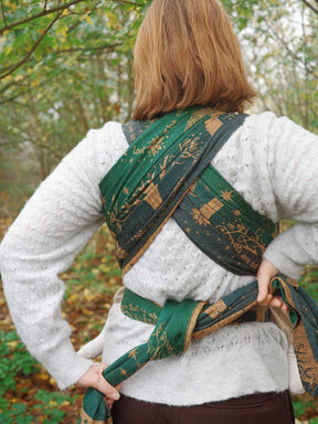 Person wearing a green patterned wrap over their shoulder in a forest setting
